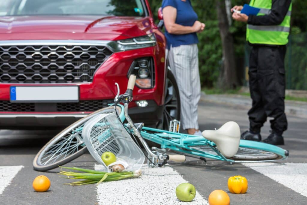 Policeman writes a ticket standing in front of a red car that hit a cyclist on a pedestrian lane