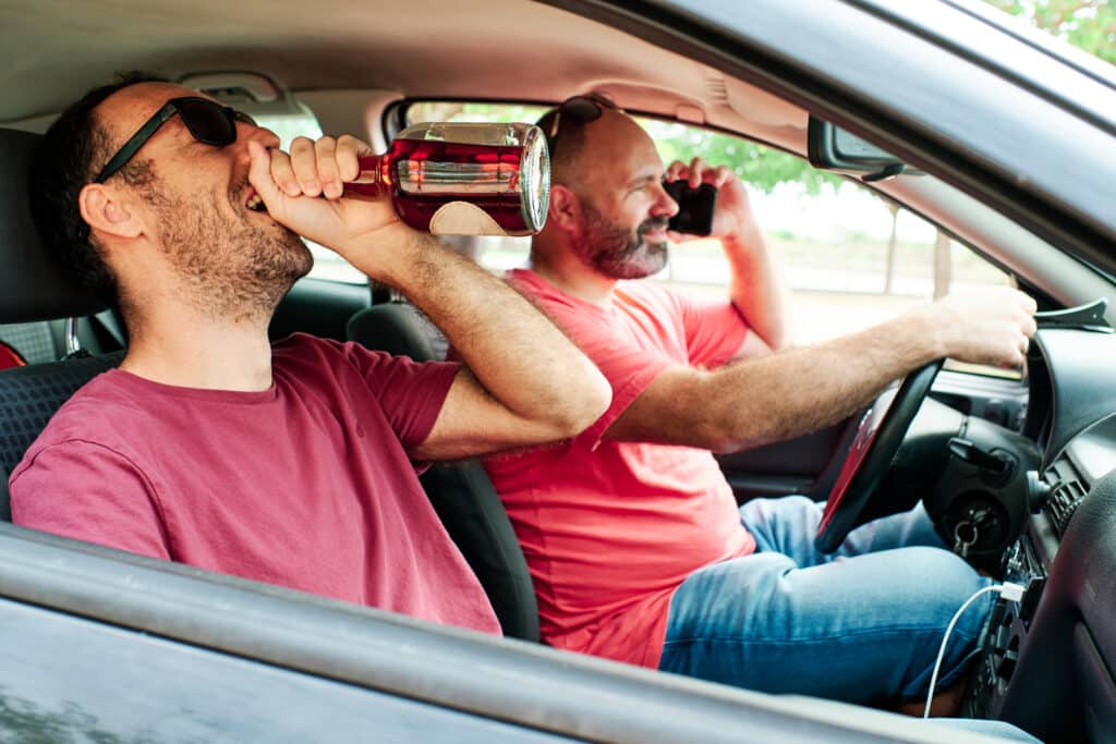 a man drinking and a driver using his mobile phone