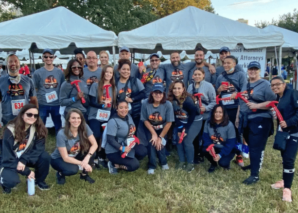 Group of smiling people wearing matching grey event t-shirts holding red cheering sticks at an outdoor event