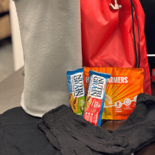 Winter care package featuring snacks, gloves, heat warmers, and fleece blanket.