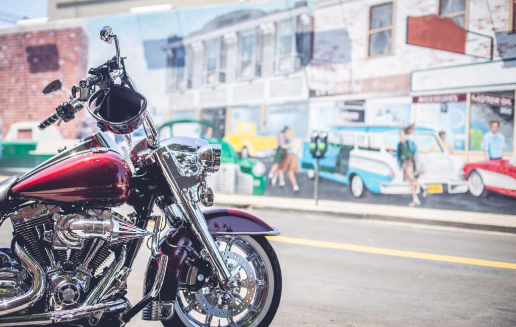Side view of red vintage custom motorcycle parked on street near wall with graffiti in USA city