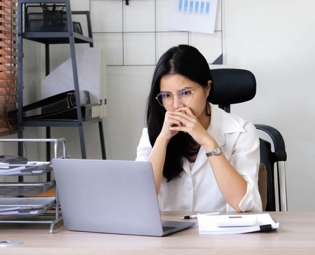 Tired female employee holding head on hand, looking at computer screen, doing hard task, having problem with computer software. Stressed exhausted businesswoman suffering from headache, feeling bored.