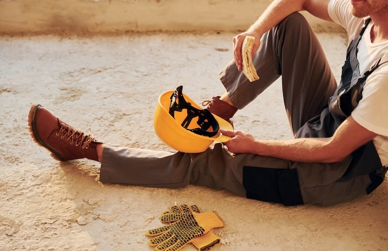 Sitting on the floor. Young man working in uniform at construction at daytime